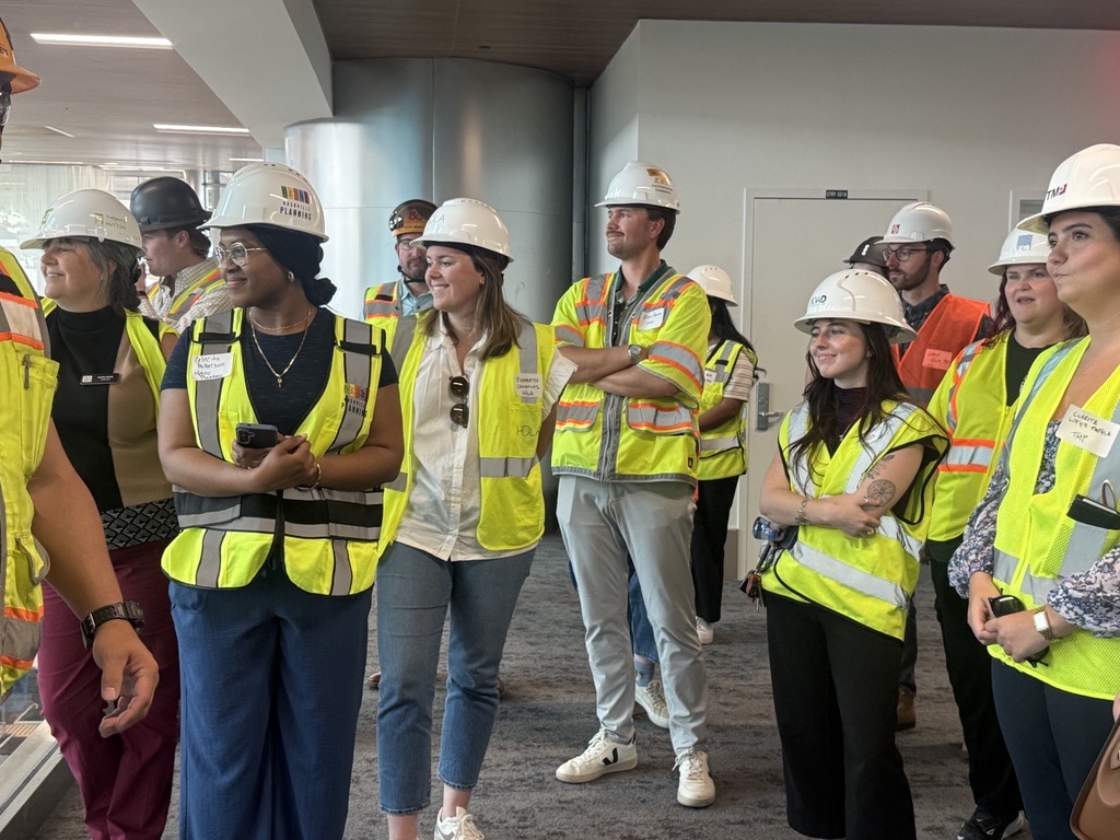 Group stands in construction gear listening to speaker.