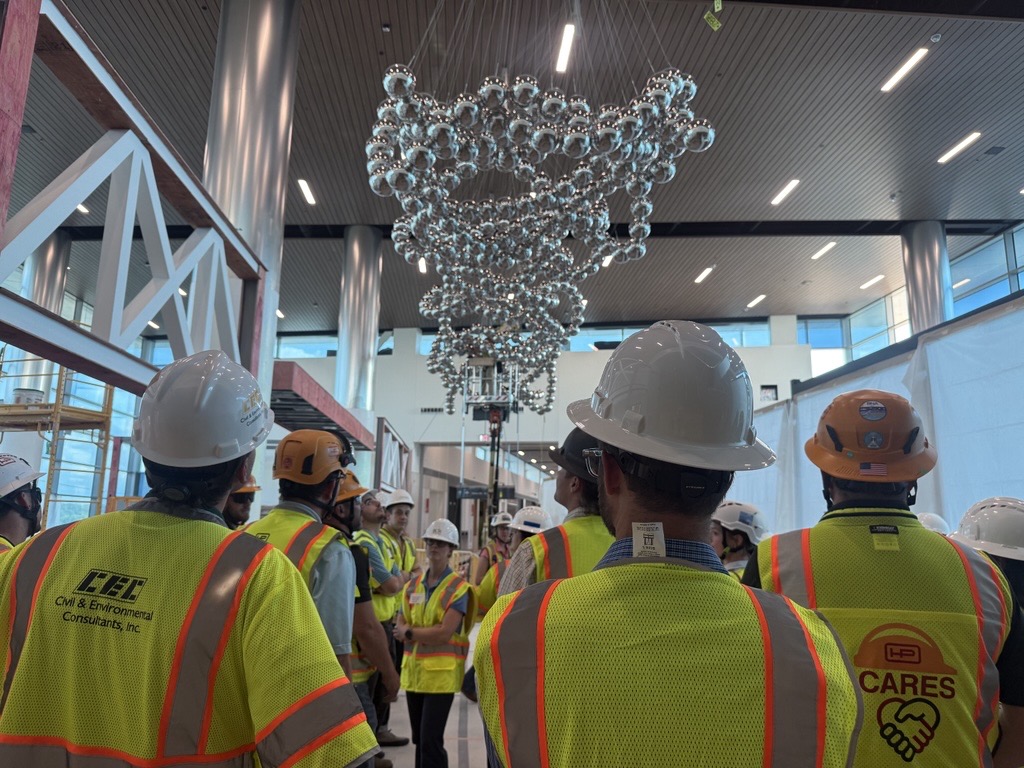 Hensel Phelps team members and project partners wearing safety gear gather inside an airport facility.