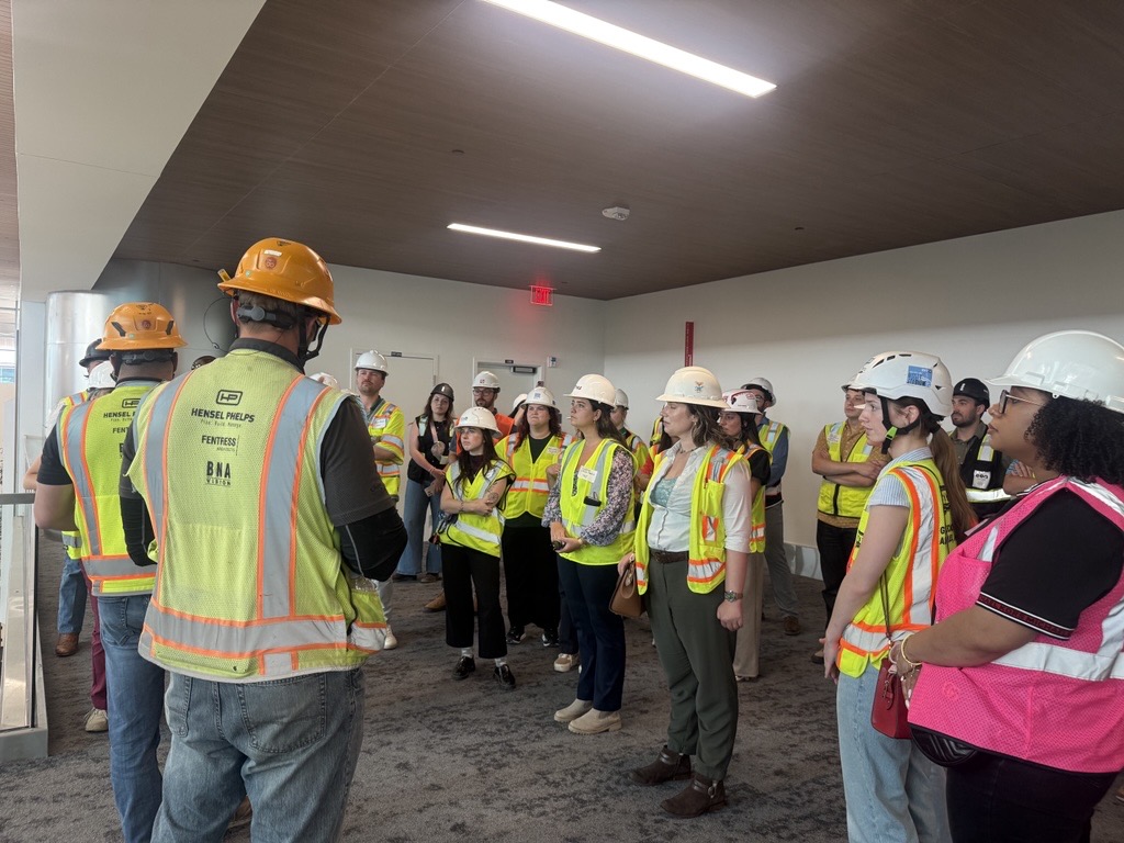 Hensel Phelps team members and project partners gather on a construction site wearing safety gear.