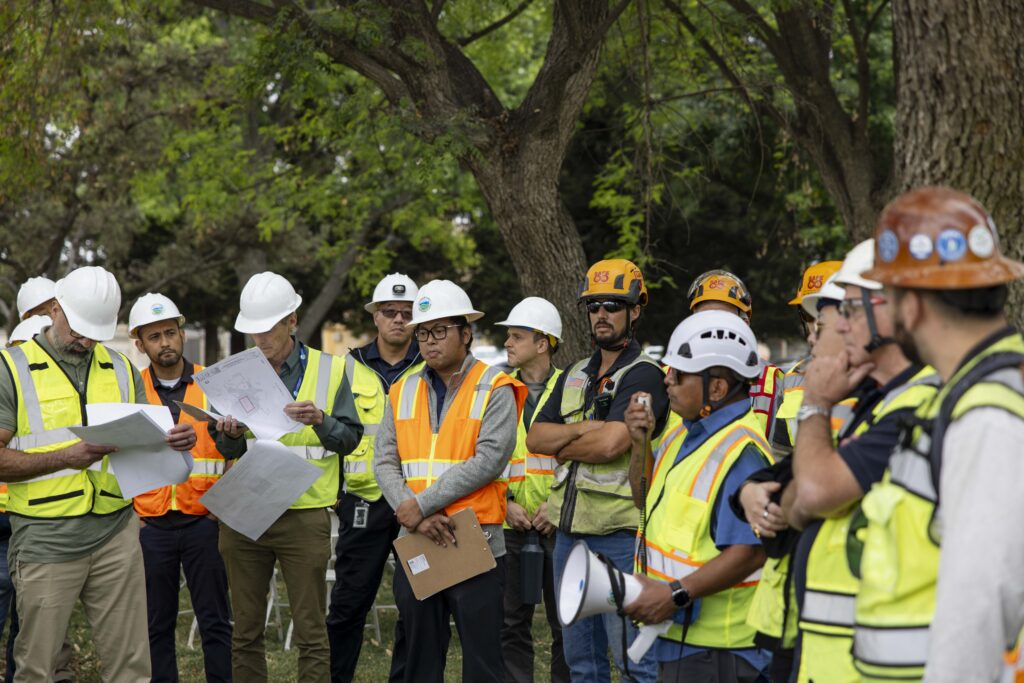 Hensel Phelps and stakeholders participating in an on-site meeting with hard hats and safety vests.