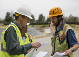 Hensel Phelps employee interacting with stakeholders wearing hard hats and safety vests.