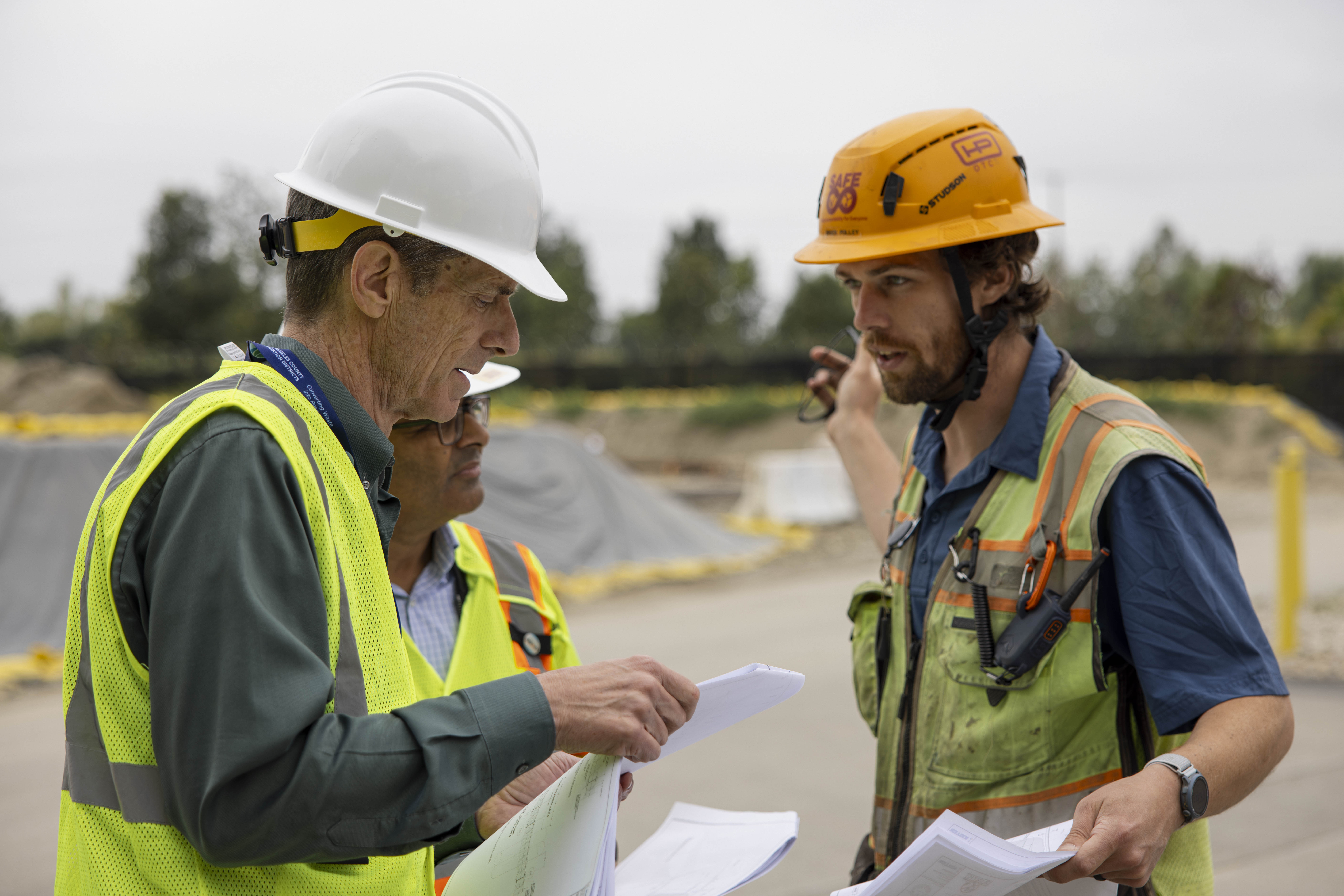 Hensel Phelps employee interacting with stakeholders wearing hard hats and safety vests.