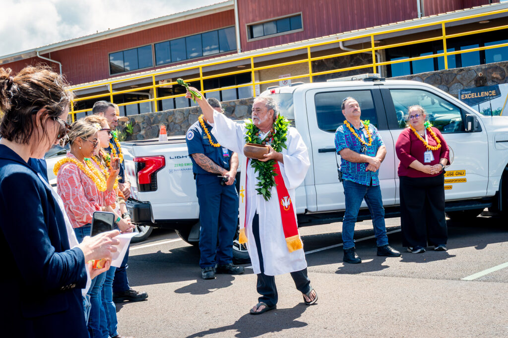 A Hawaiian kahu conducts a pī kai ceremony, sprinkling blessed water to purify and bless the new EV charging station at Kapalua Airport in Lahaina