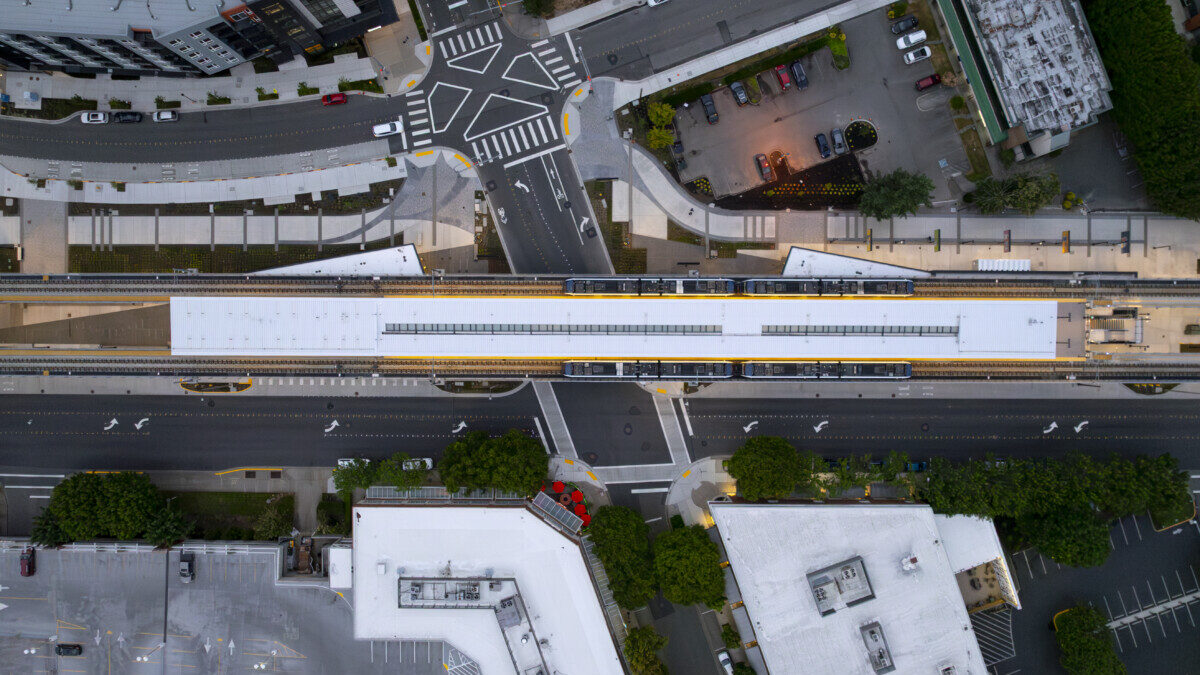 Aerial view of the Sound Transit Downtown Redmond Link Extension and light rail train surrounded by buildings, trees and distant mountains.