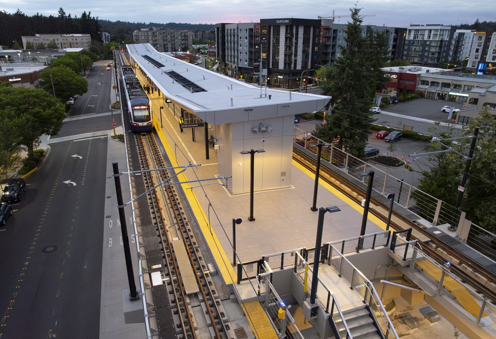 Elevated Downtown Redmond Link Extension station with a light rail train at the platform, surrounded by streets, trees and residential buildings.