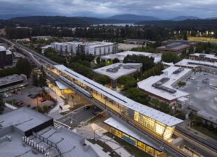 Aerial view of the Sound Transit Downtown Redmond Link Extension and light rail train surrounded by buildings, trees and distant mountains.