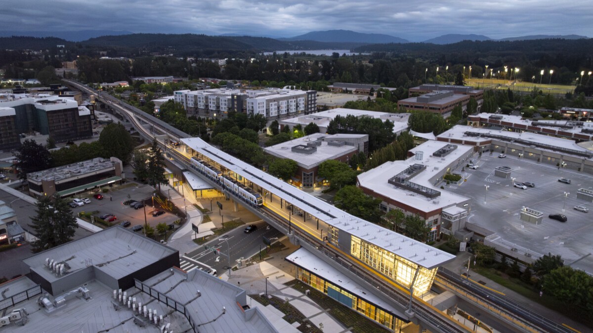 Aerial view of the Sound Transit Downtown Redmond Link Extension and light rail train surrounded by buildings, trees and distant mountains.